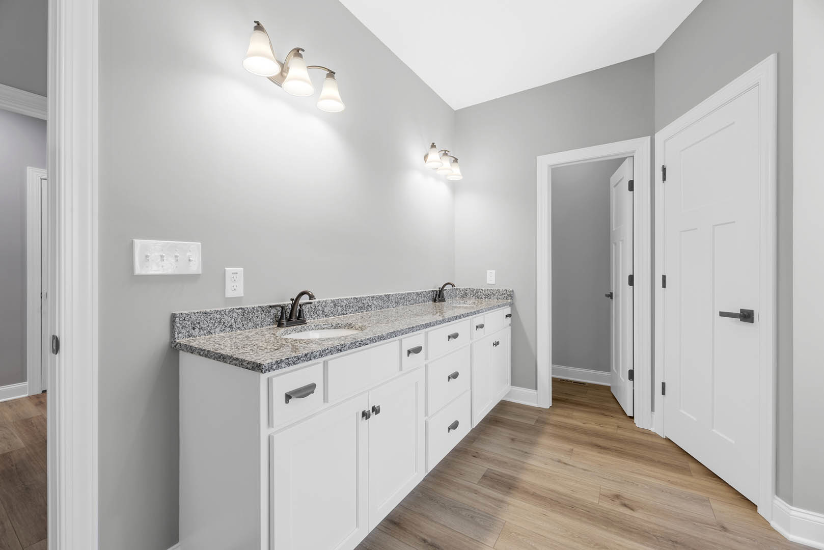 Bathroom featuring white cabinets, marble countertops, three-light fixture above mirror, white rectangular vent, white door with black handle, tile flooring, and undermount sink.