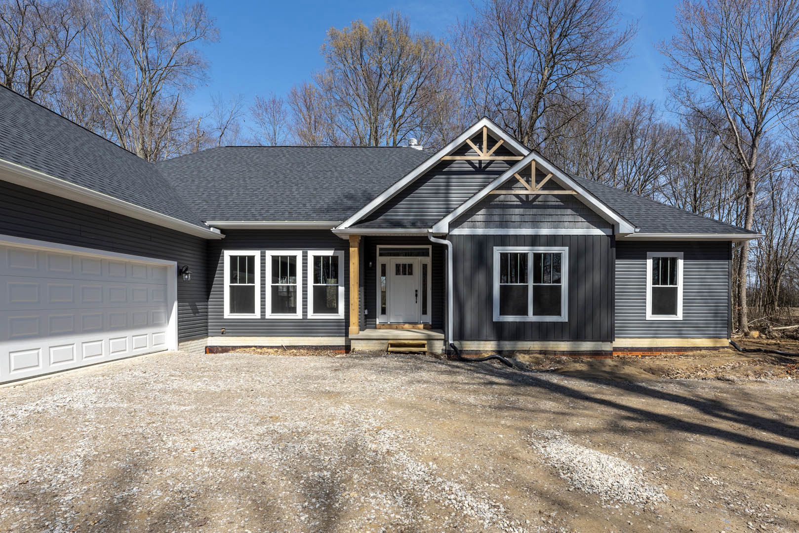 Two-story home with light siding, white-framed windows, white front door with glass panel, gravel driveway, mature trees in background