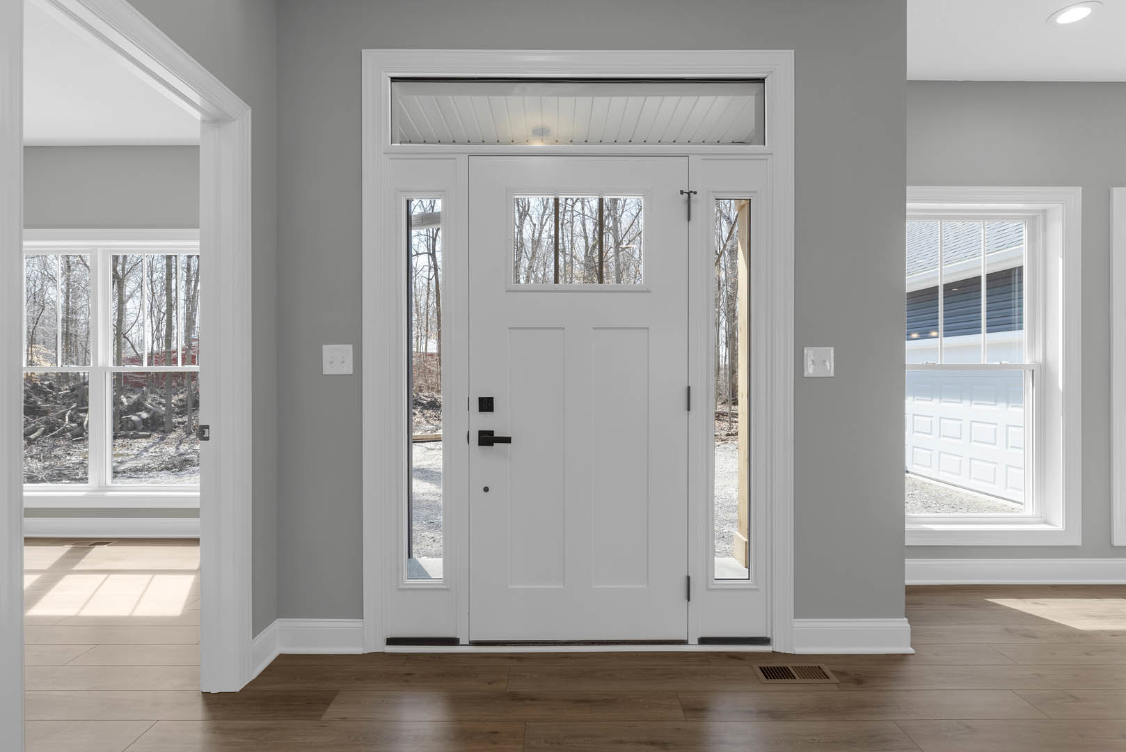 White paneled door with frosted glass window, white light switch on gray wall, wood flooring, and white baseboards