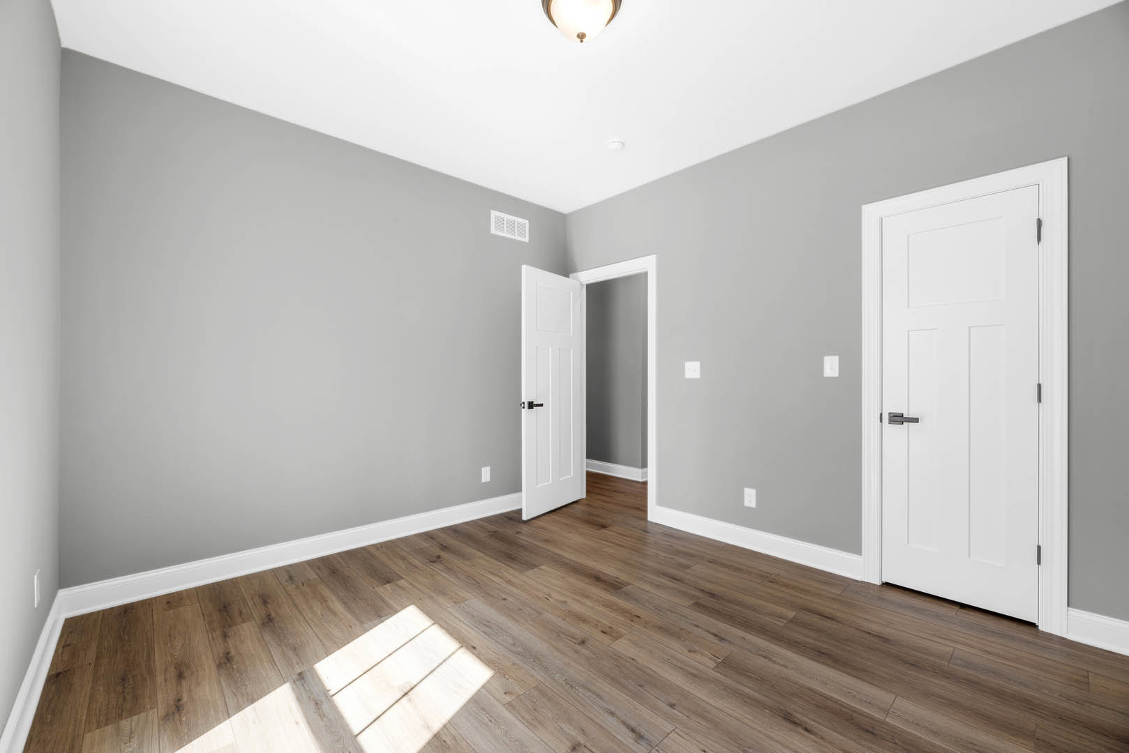 White paneled doors with black handles, hardwood floors with white baseboard trim, recessed ceiling light illuminating the space