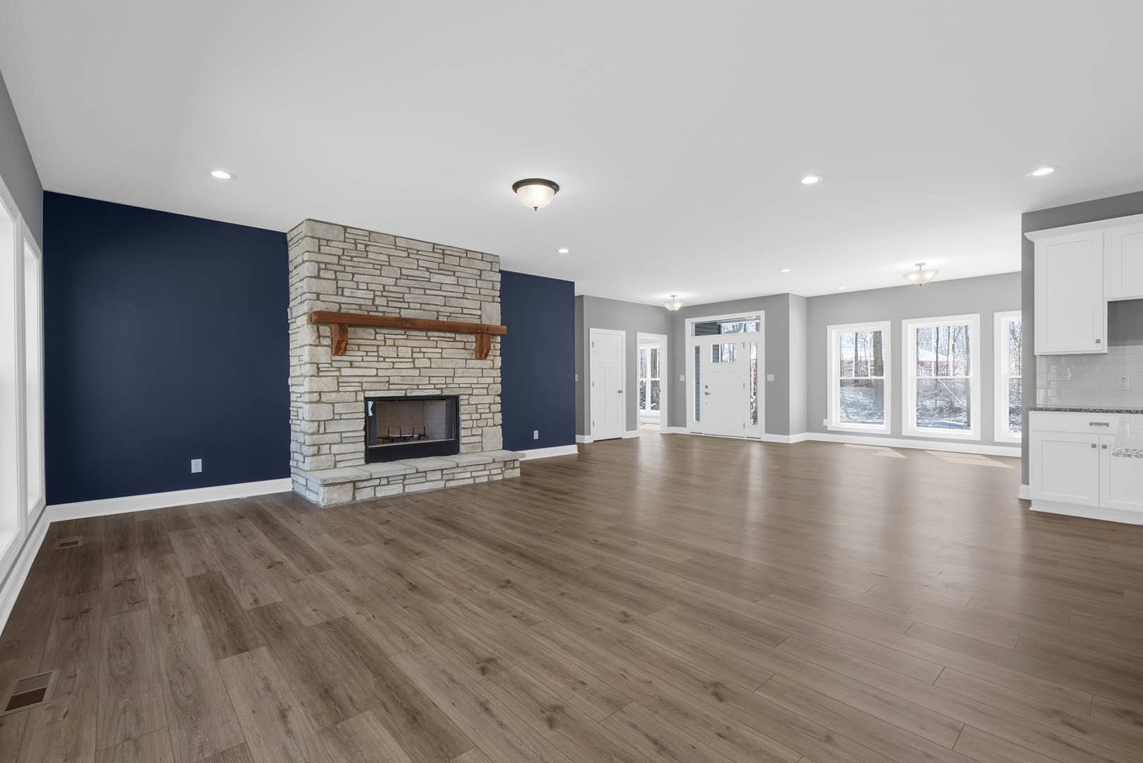 Spacious living area with hardwood flooring, central fireplace, white plaster walls, ceiling light fixture, glass-paneled door, and window nook with table and chairs