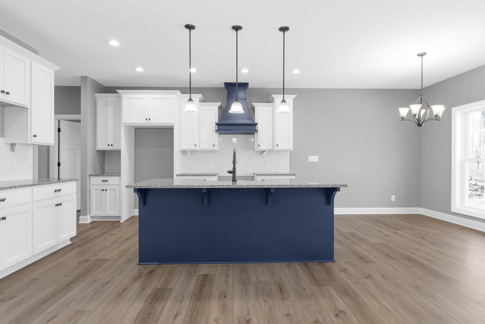 Blue kitchen island with white countertop and built-in sink, wood flooring, blue cabinetry, bell-shaped chandelier, and light blue accent wall.