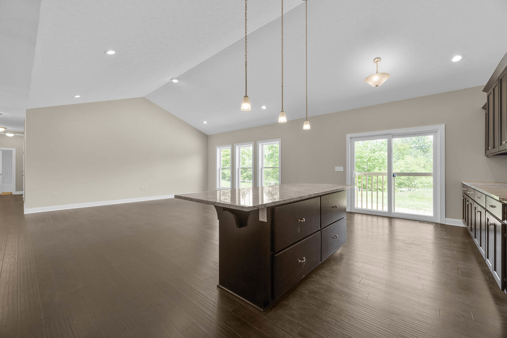 Large kitchen with marble-topped island featuring drawers, white cabinetry, laminate flooring, sliding glass door with white frame, and ceiling light fixture.