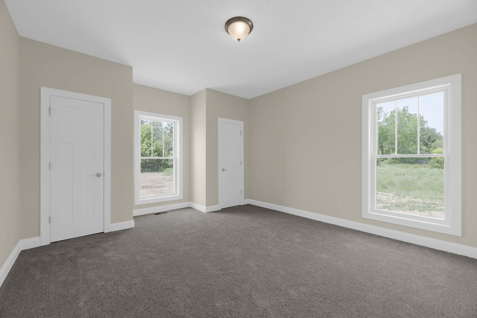 Carpeted room featuring a white door with a silver handle, large windows overlooking a field and trees, plaster walls, and a ceiling light fixture