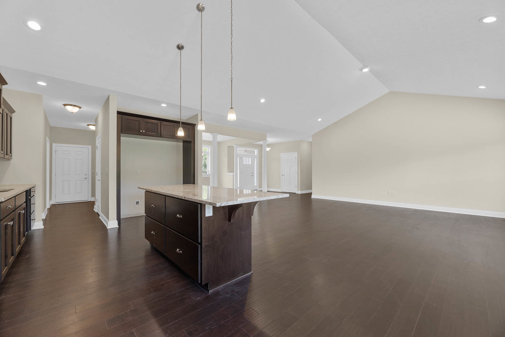 Spacious open floor plan featuring a kitchen island with marble countertop, white cabinetry with silver handles, light wood flooring, and modern fixtures