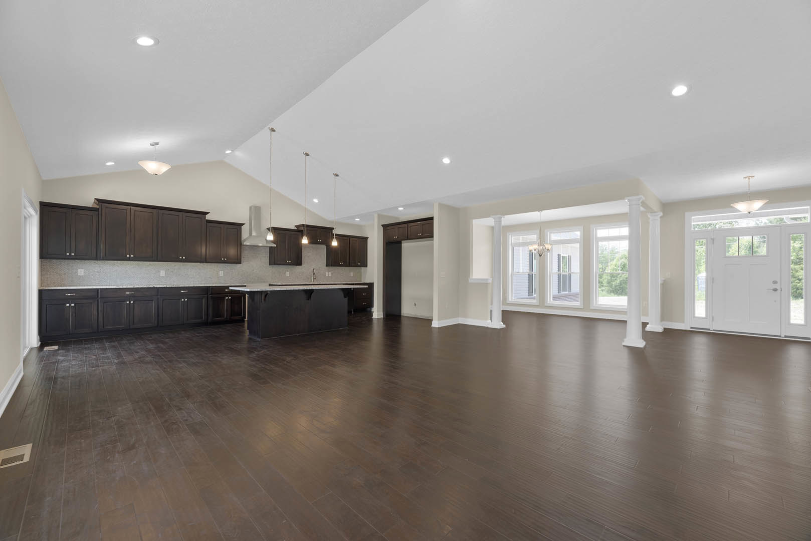 Spacious room with dark wood floors, open kitchen area, white paneled door with glass inserts, recessed ceiling lights, ceiling vent, and white plaster walls and ceiling