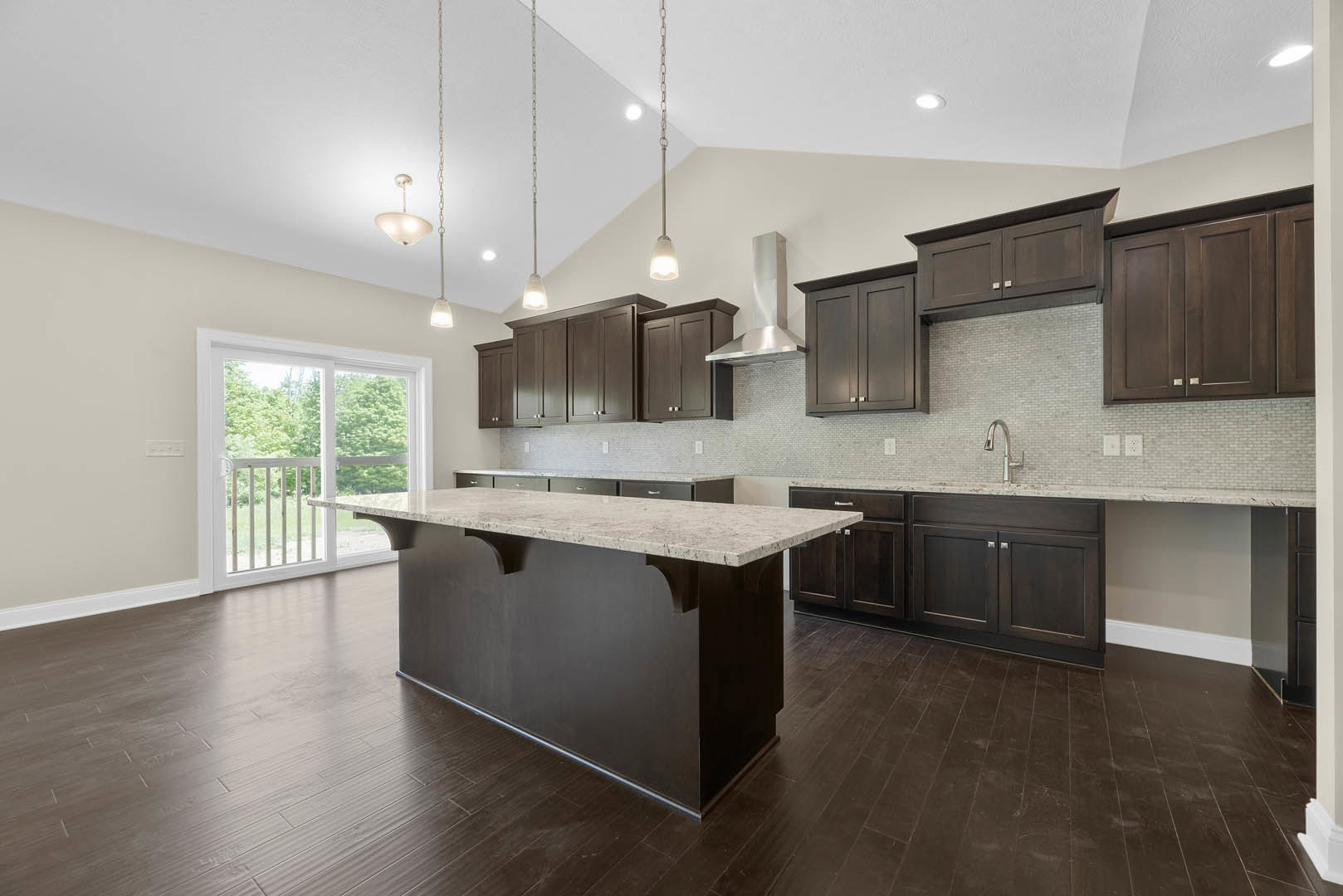 Kitchen with dark wood cabinetry, marble-topped island, tile flooring, stainless steel sink, and sliding glass door leading to dining area