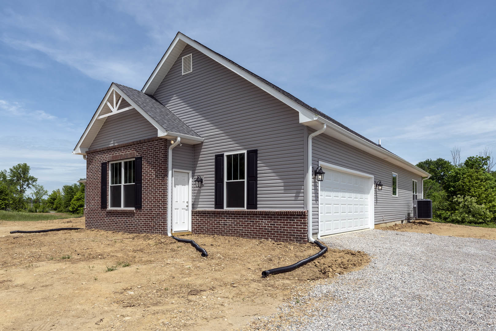 White siding house with attached garage, black outdoor lamp above white garage door, white-framed window, trees and cloudy sky in background