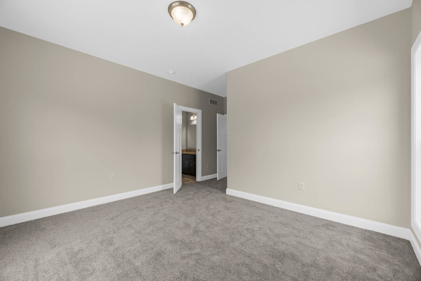Carpeted bedroom with white walls, open door leading to bathroom featuring marble countertop, black cabinet, and modern ceiling light fixture