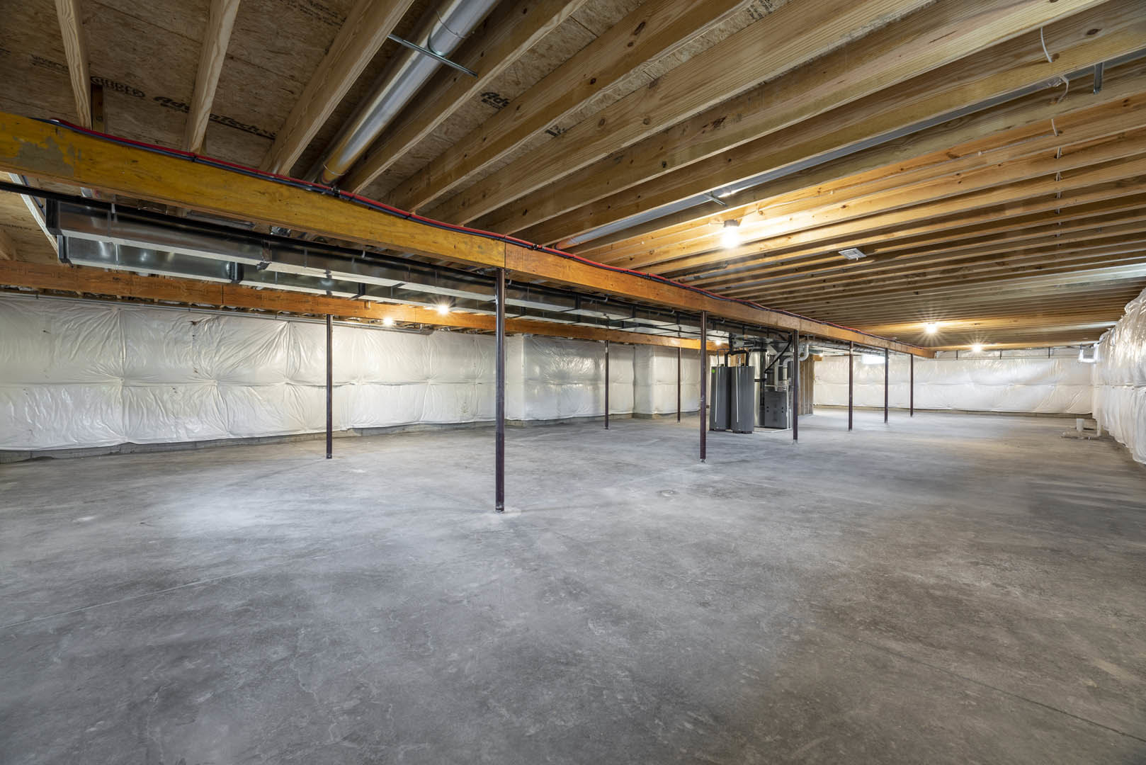 Wooden ceiling with exposed beams and metal pipes, concrete floor, white walls, empty basement interior