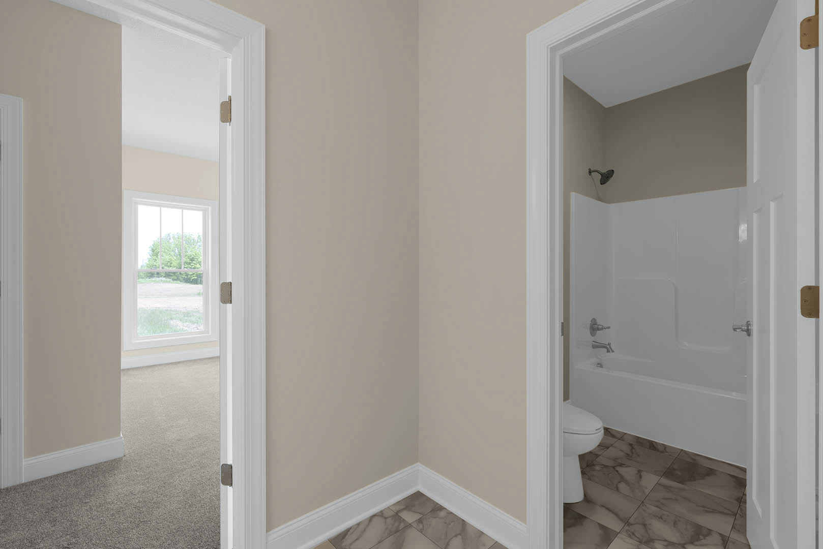 White bathtub with silver faucets next to a toilet, light-colored walls, window overlooking trees, carpeted flooring