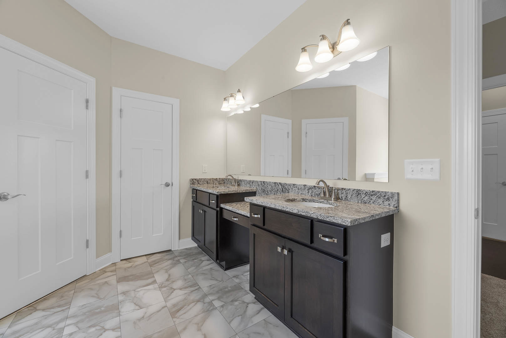 Bathroom with polished marble floor, double vanity with marble countertop, white cabinetry, silver hardware, and three-light fixture above sinks.