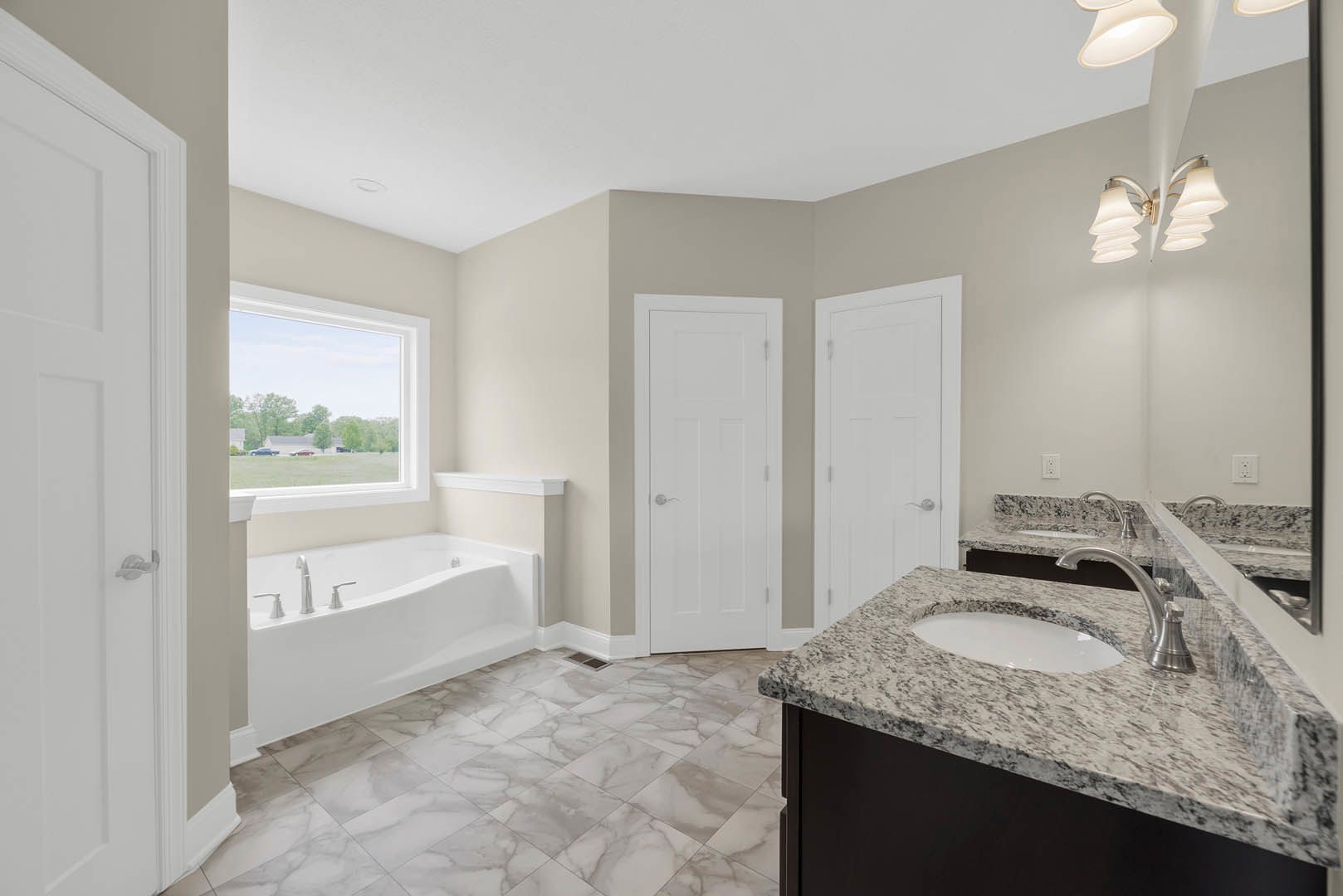 Bathroom featuring marble countertops, white oval sink, silver faucet, freestanding bathtub with chrome fixtures, white tile floor, white door with silver handle, window