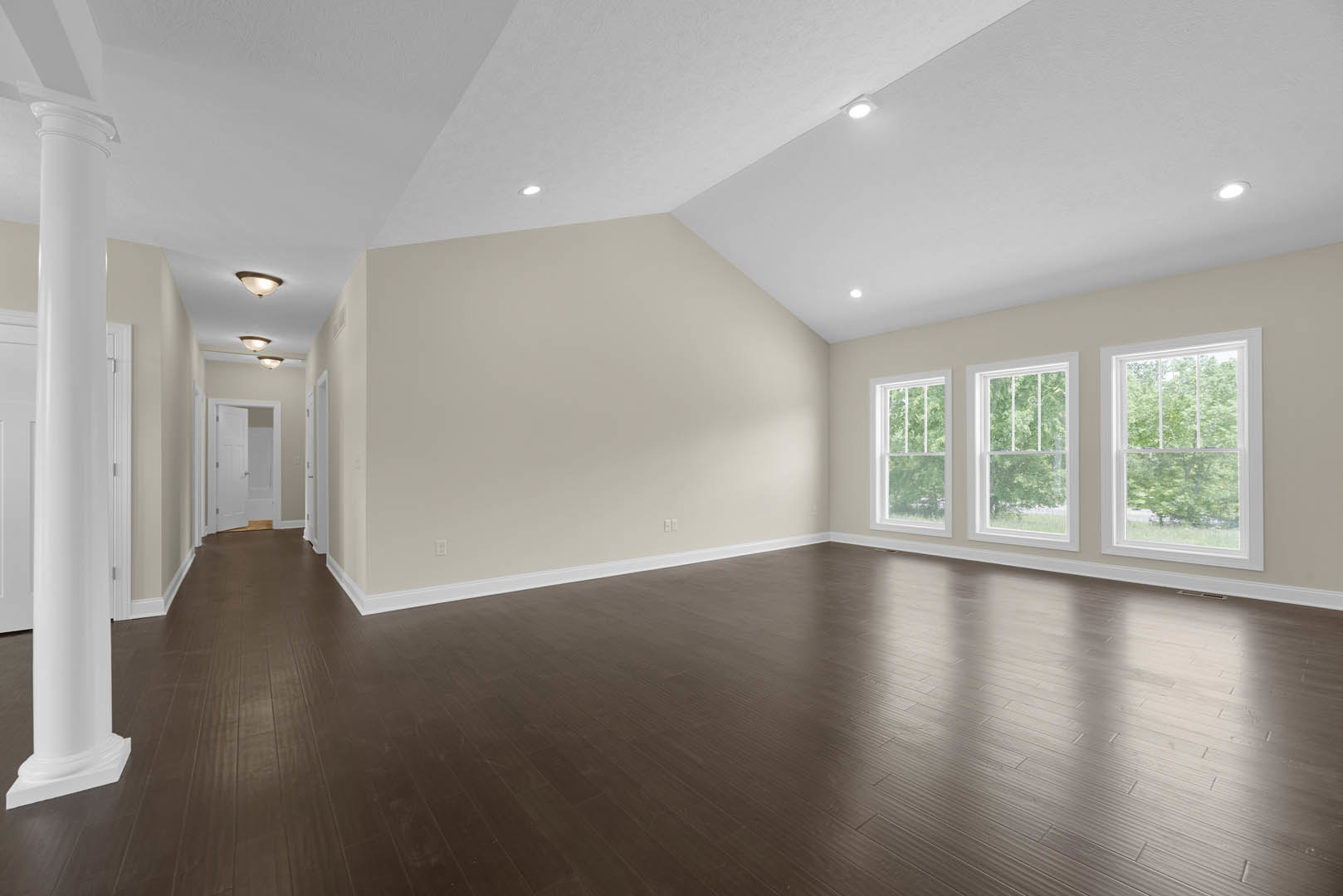 Dark wood flooring, white plaster walls, row of large windows with white frames, view of trees outside, white cylindrical object with black handle near wall.