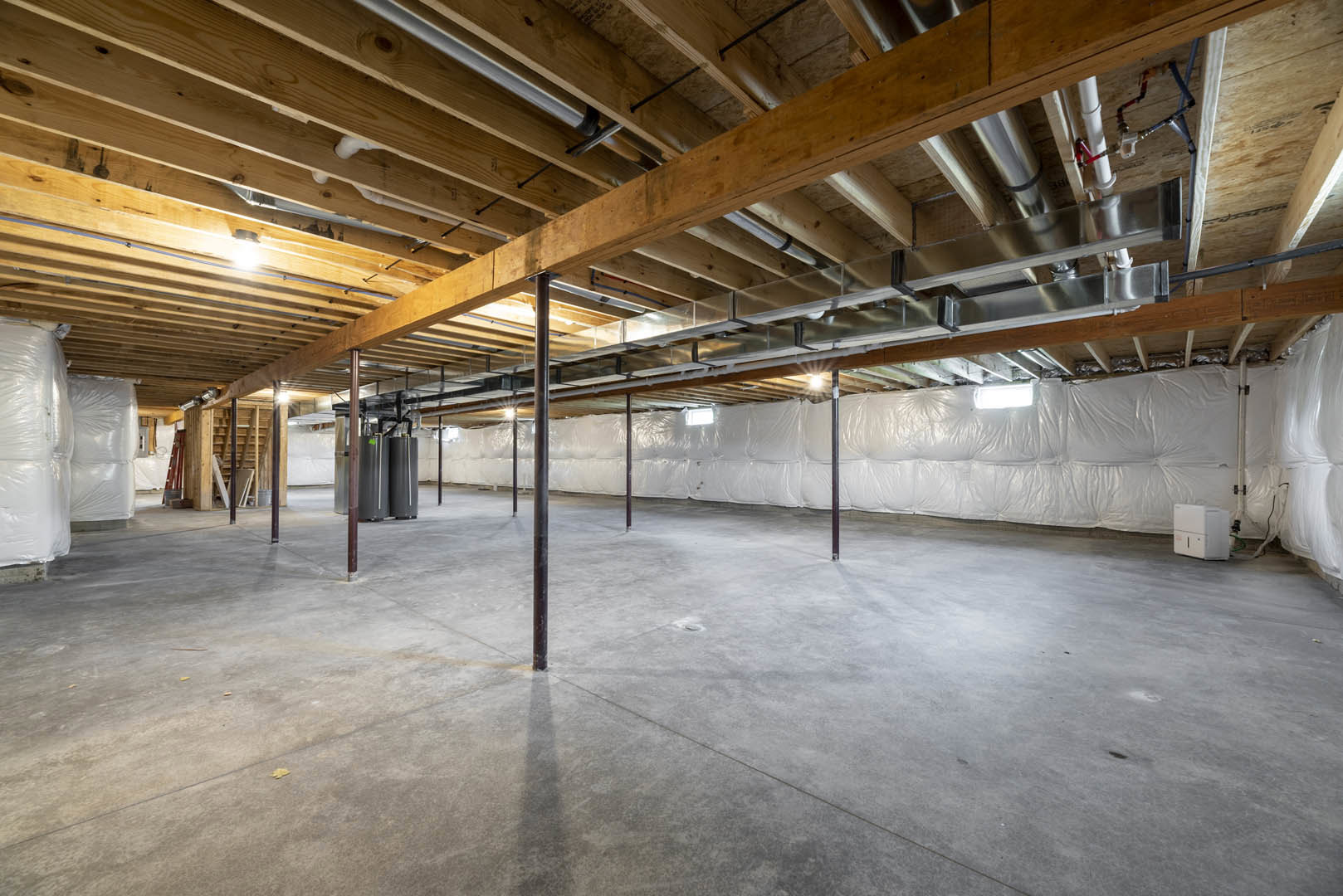 Unfinished basement with exposed wooden beams, steel pipes, concrete floor, and several white bags placed on the ground