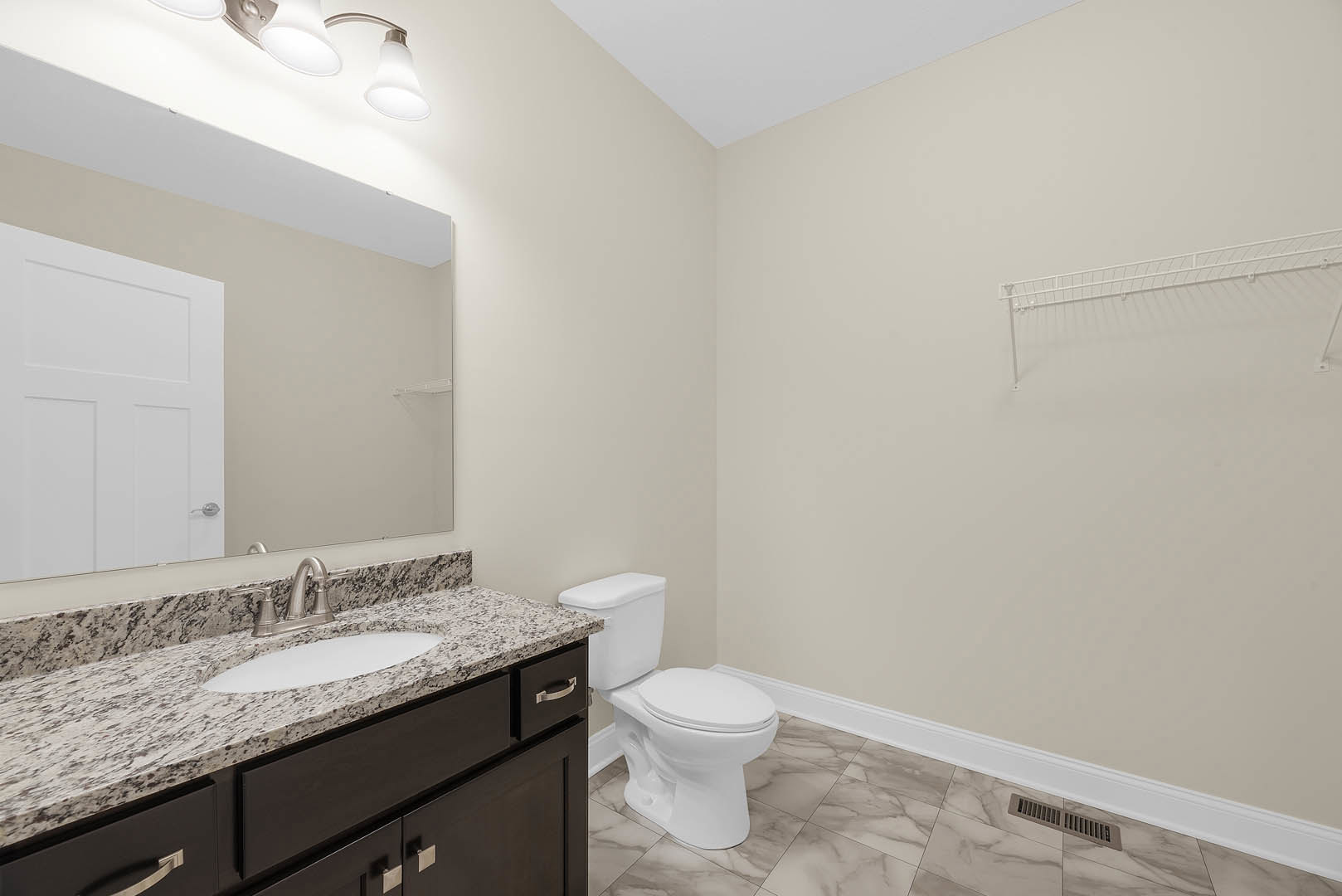 Marble countertop with undermount sink, white cabinetry, toilet, tiled floor, white door with silver handle, wall-mounted white shelf