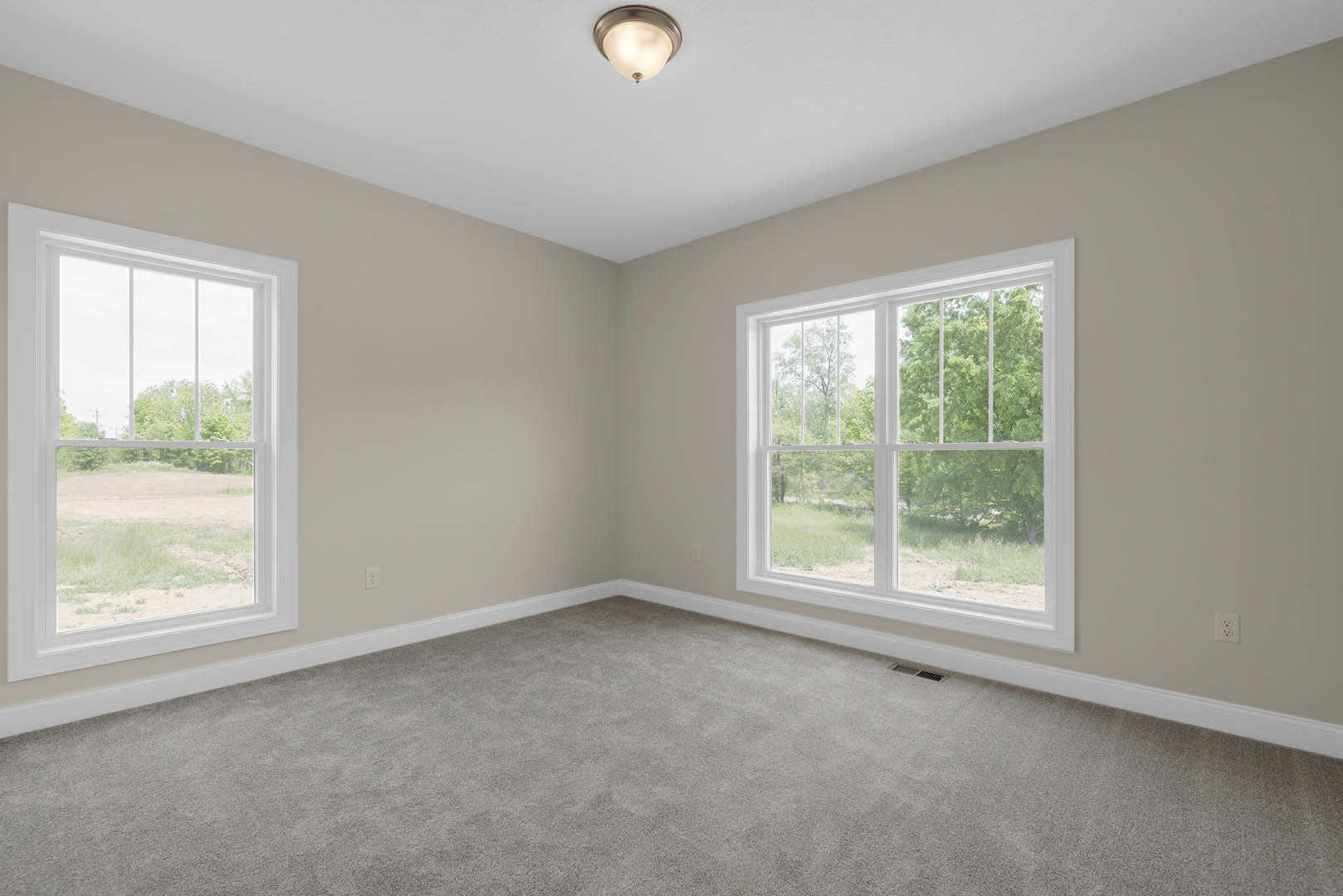 Carpeted room with white walls, large windows overlooking trees and a grassy field, ceiling light fixture, simple molding trim