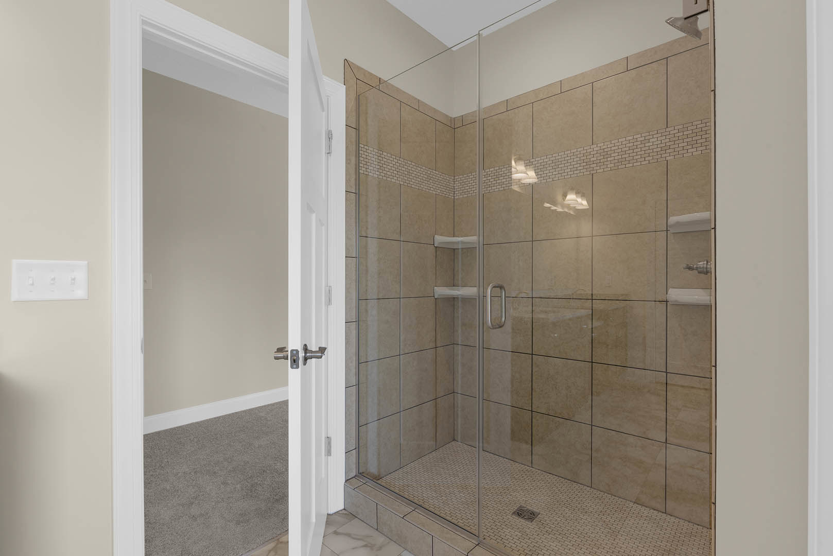 Bathroom featuring a glass-enclosed shower with tile walls, white rectangular wall switch, white framed wall, and visible shower drain on the floor