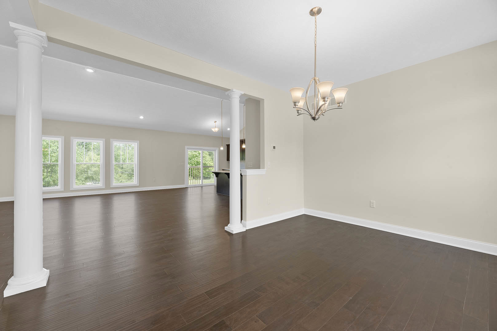 Brown hardwood floor with white columns, large white pillar, ornate chandelier, white-framed window overlooking trees, plaster walls, and ceiling molding