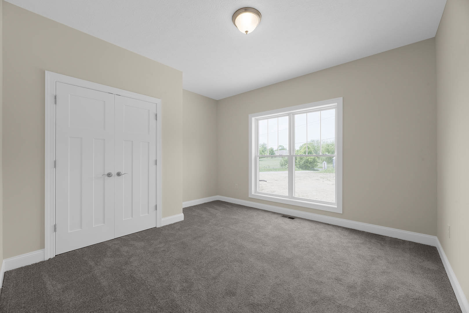 Carpeted room with white paneled door featuring silver handles, large window overlooking grassy field, ceiling-mounted light fixture, white walls with crown molding