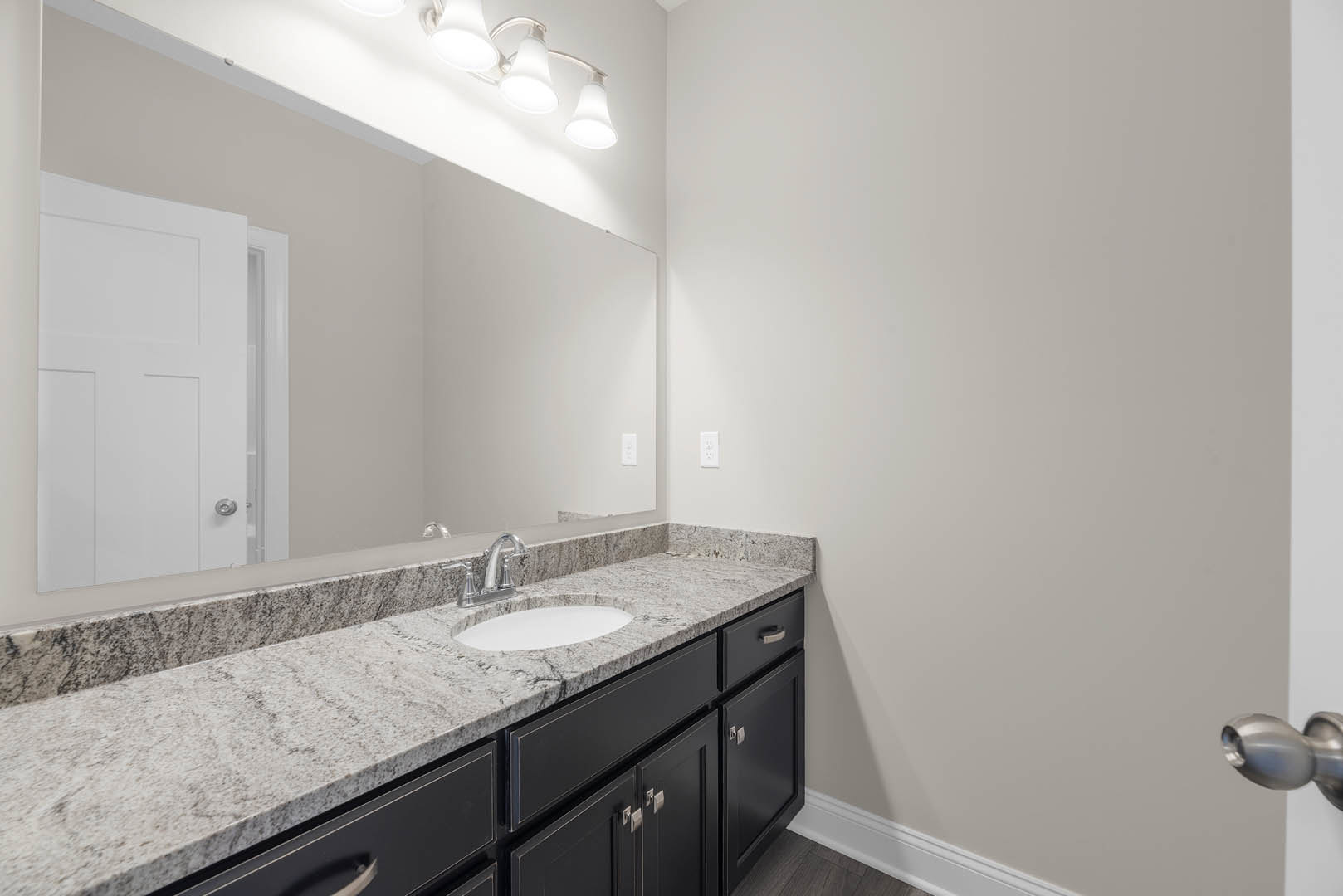 Bathroom featuring a marble countertop with an undermount sink, chrome faucet, large wall mirror, white door with silver handle, and modern light fixture above the vanity