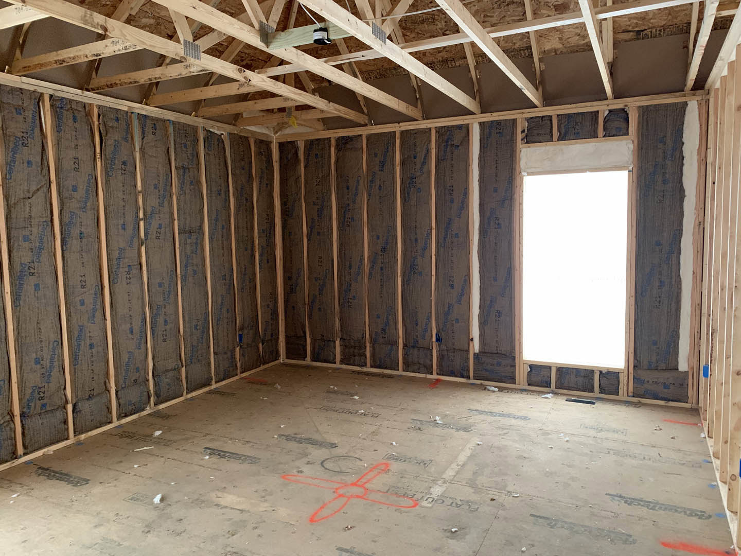 Living room with exposed wood ceiling beams, large window, white walls, and red-painted floor