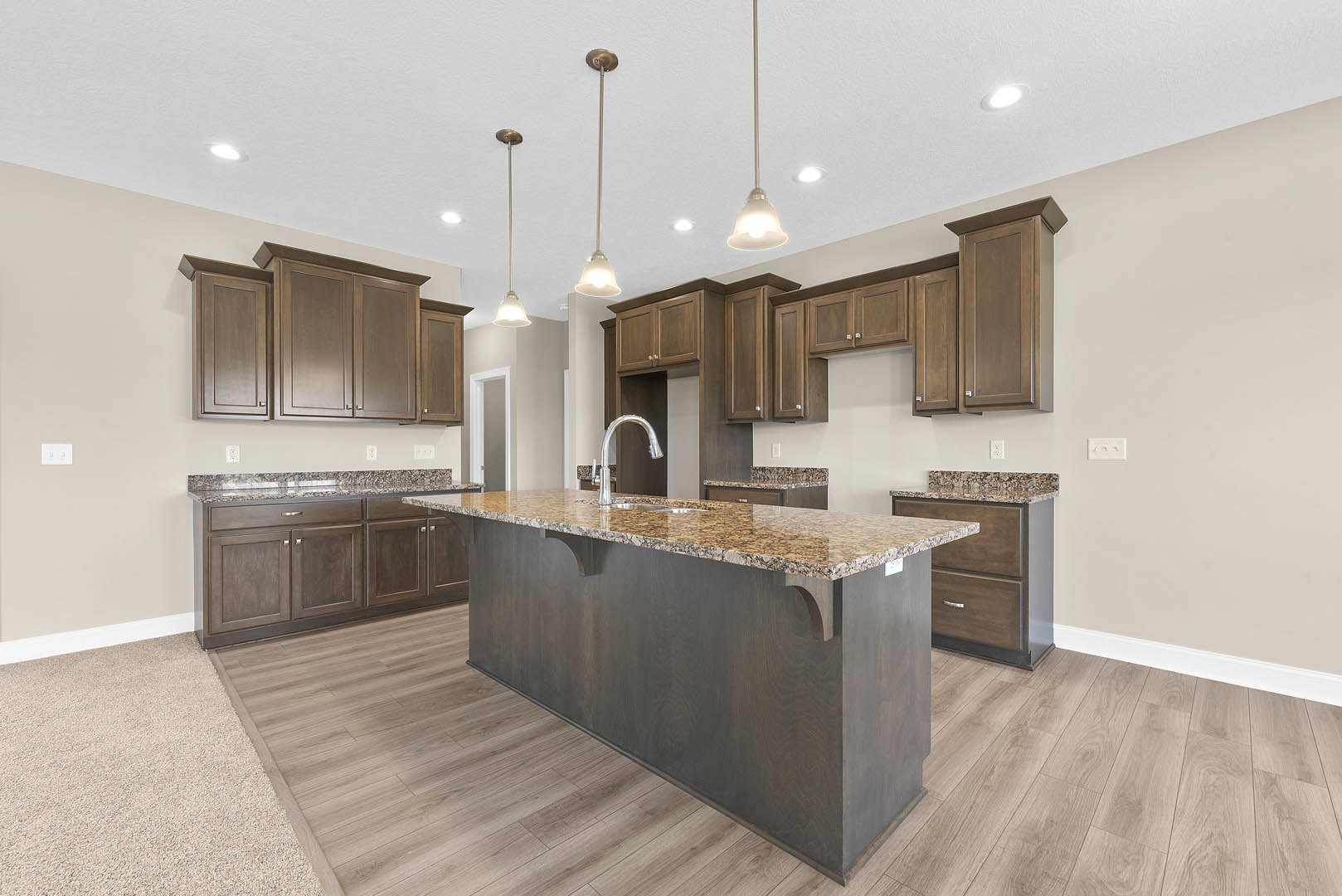 Spacious kitchen featuring a large central island with granite countertops, white cabinetry, tile backsplash, stainless steel sink, and hardwood flooring.
