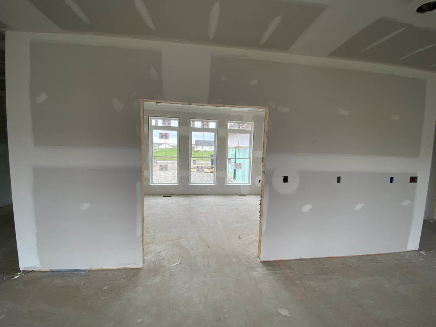 White-walled room featuring a row of windows with signage, light-colored flooring, and a door; windows overlook a grassy field.