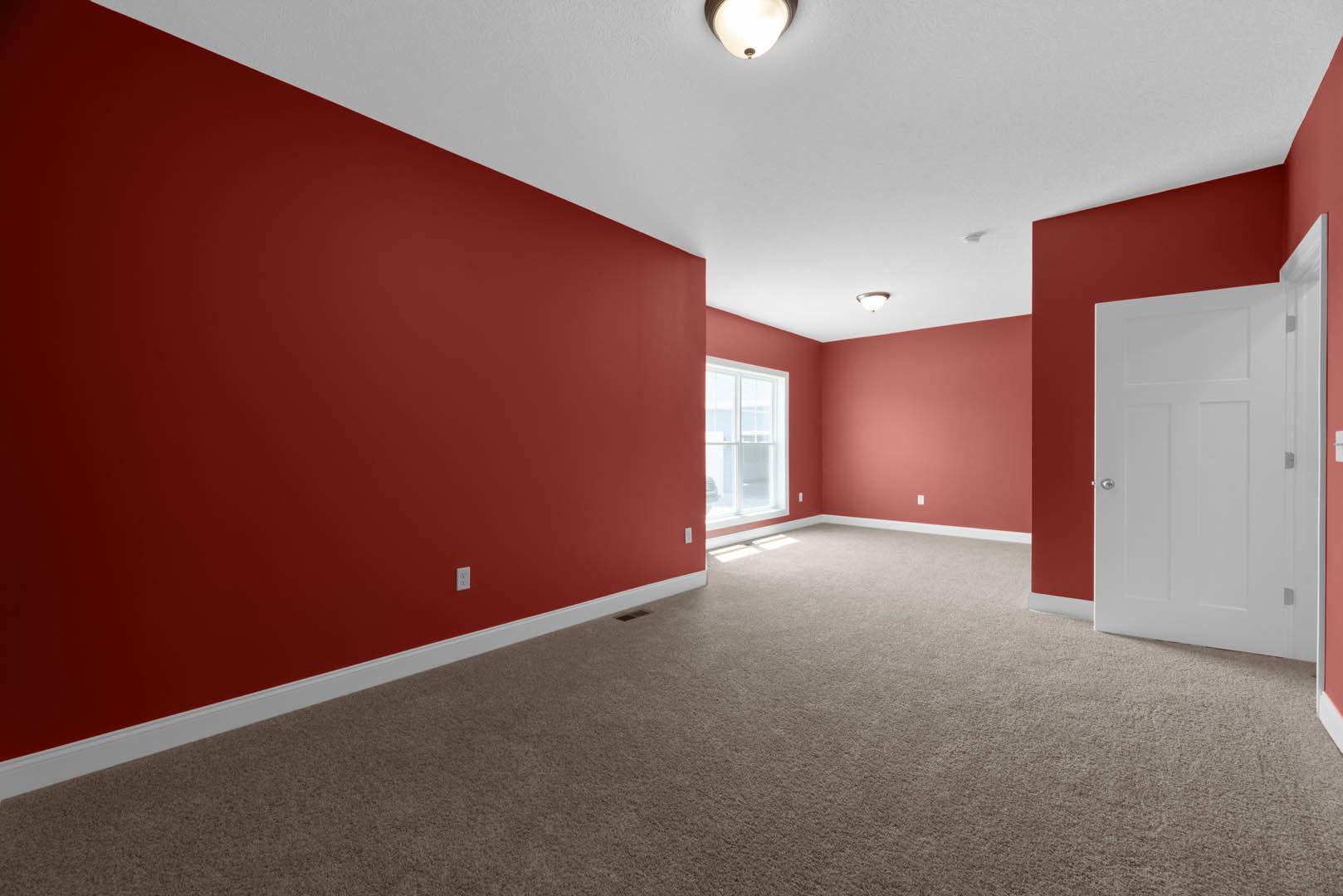 Red-walled room with matching red carpet, window featuring a red frame, white door with silver knobs, ceiling light fixture, plaster ceiling and walls