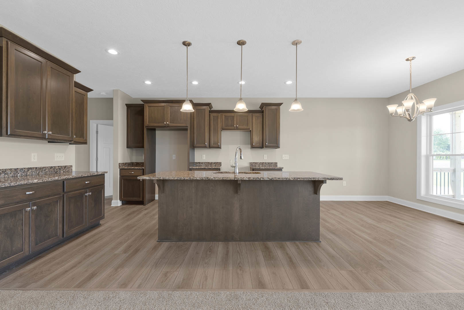 Open kitchen with granite island, stainless steel sink, wood flooring, white cabinetry, and large window overlooking green lawn