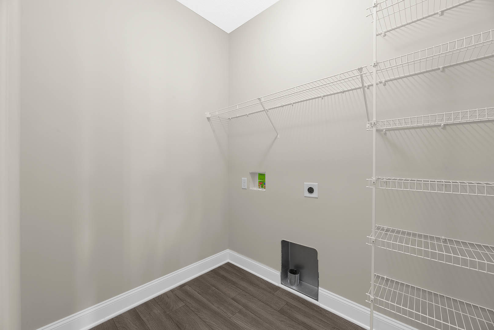 White shelf with metal racks mounted on a plaster wall, wood floor with white baseboard, white wall outlet featuring a round black circle, metal cylinder in the corner, white wire