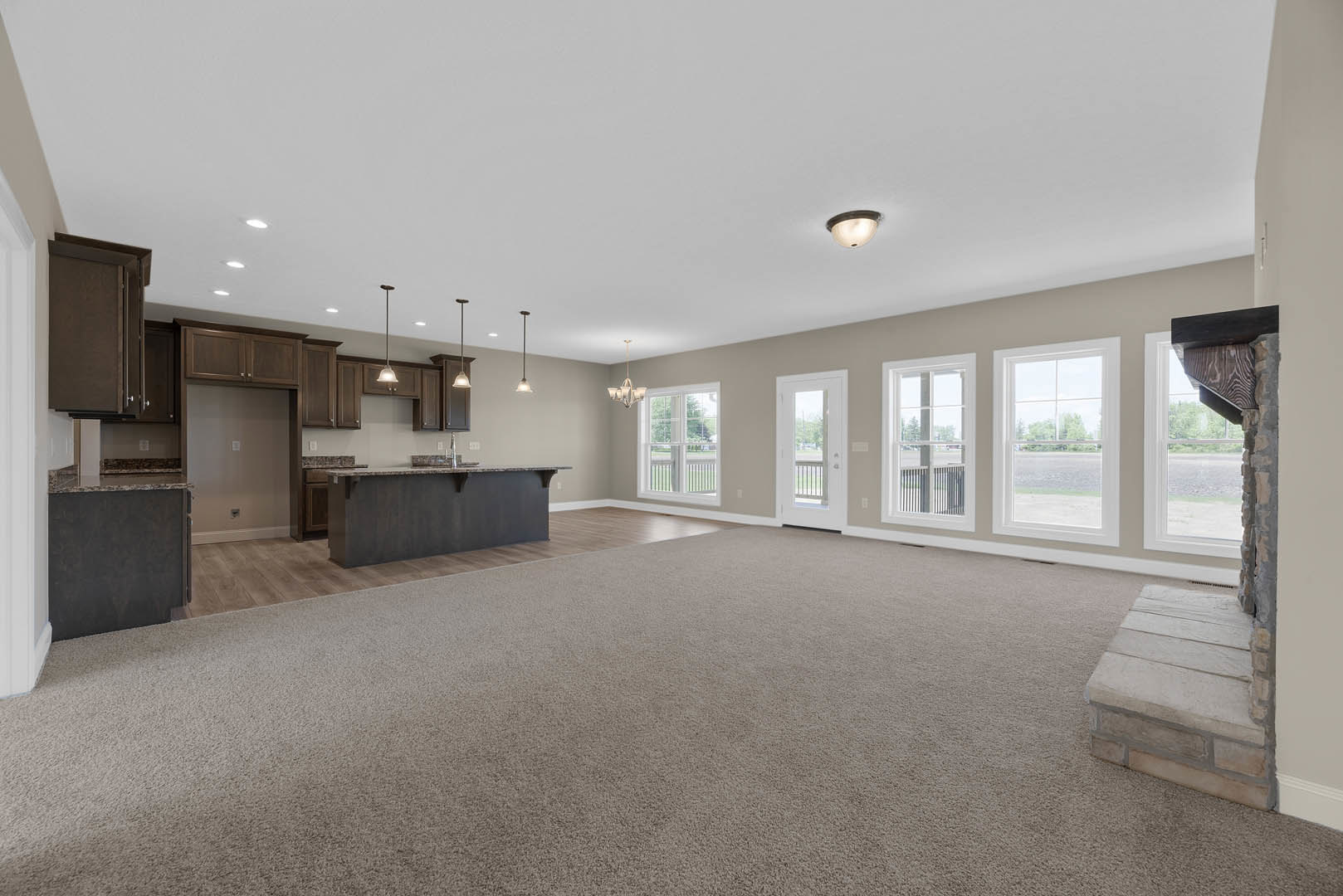 Open-concept room featuring a modern kitchen with white cabinetry, a bar with seating, recessed ceiling lights, large window with outdoor view, carpeted floor, and a white door