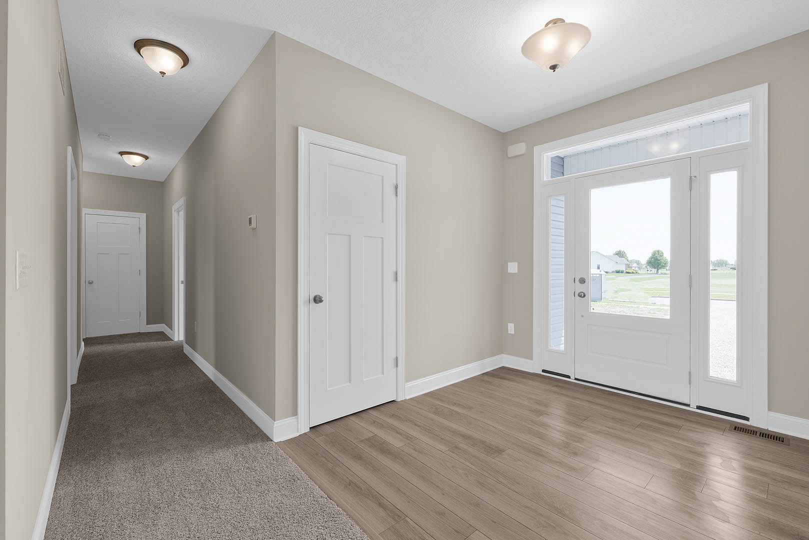 Hallway with white paneled doors, silver door knobs, wood flooring, white walls, ceiling light fixture, and a glass window inset in one door