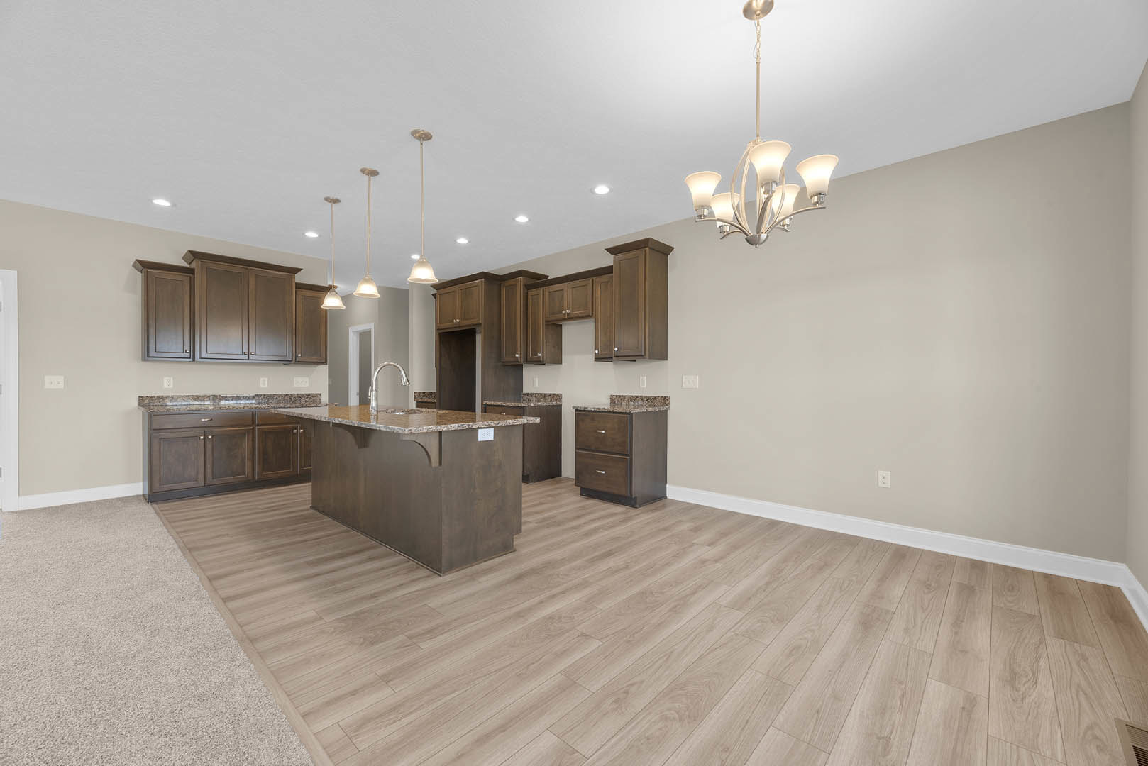 Kitchen with wood flooring, white baseboards, marble island countertop, silver faucet, cabinetry, and ornate chandelier hanging from ceiling
