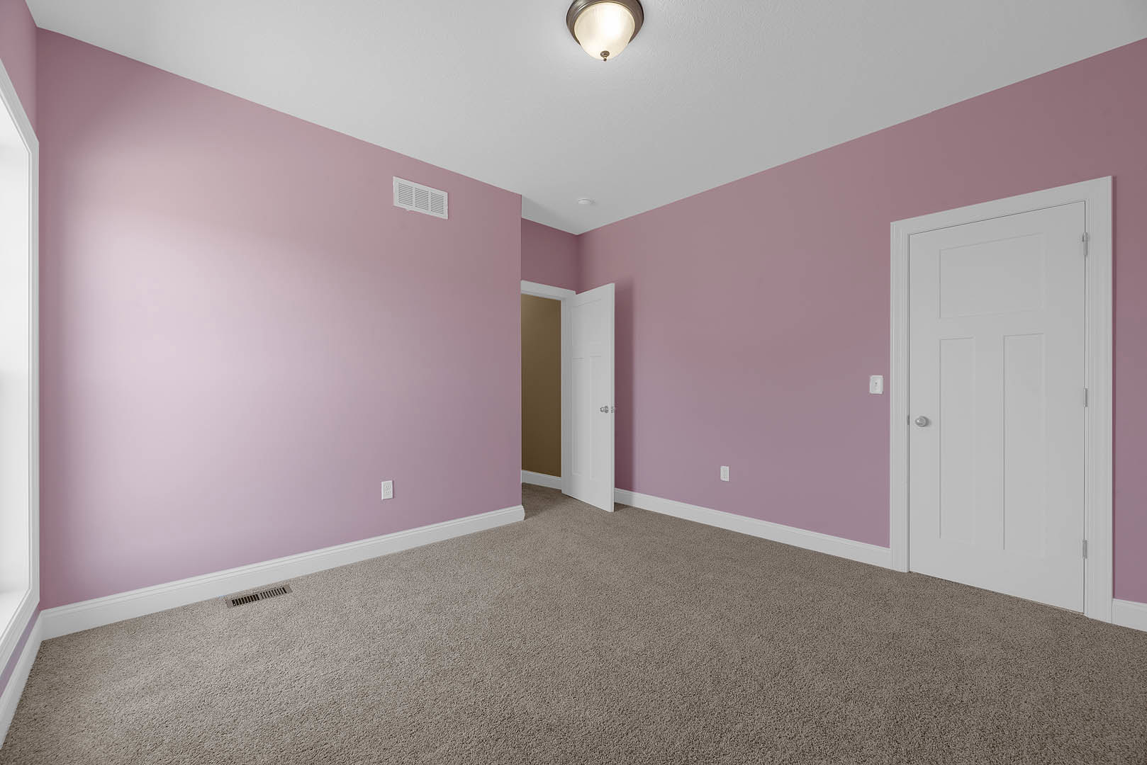 Carpeted room with soft pink walls, white door, ceiling light fixture, wall vent, and crown molding