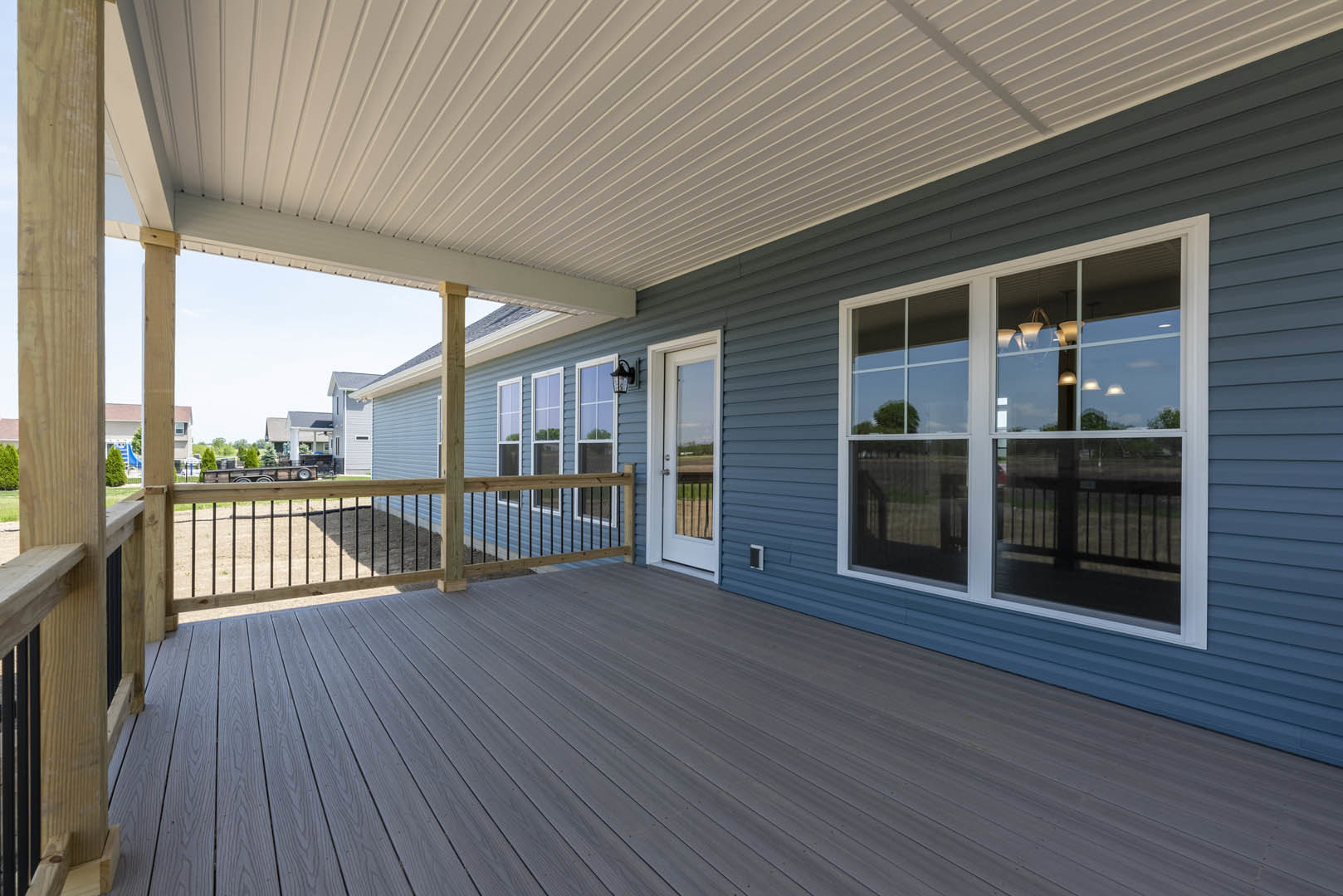 Wooden deck with two covered porches, white railings, multiple windows, exterior light fixture, and view of open field.