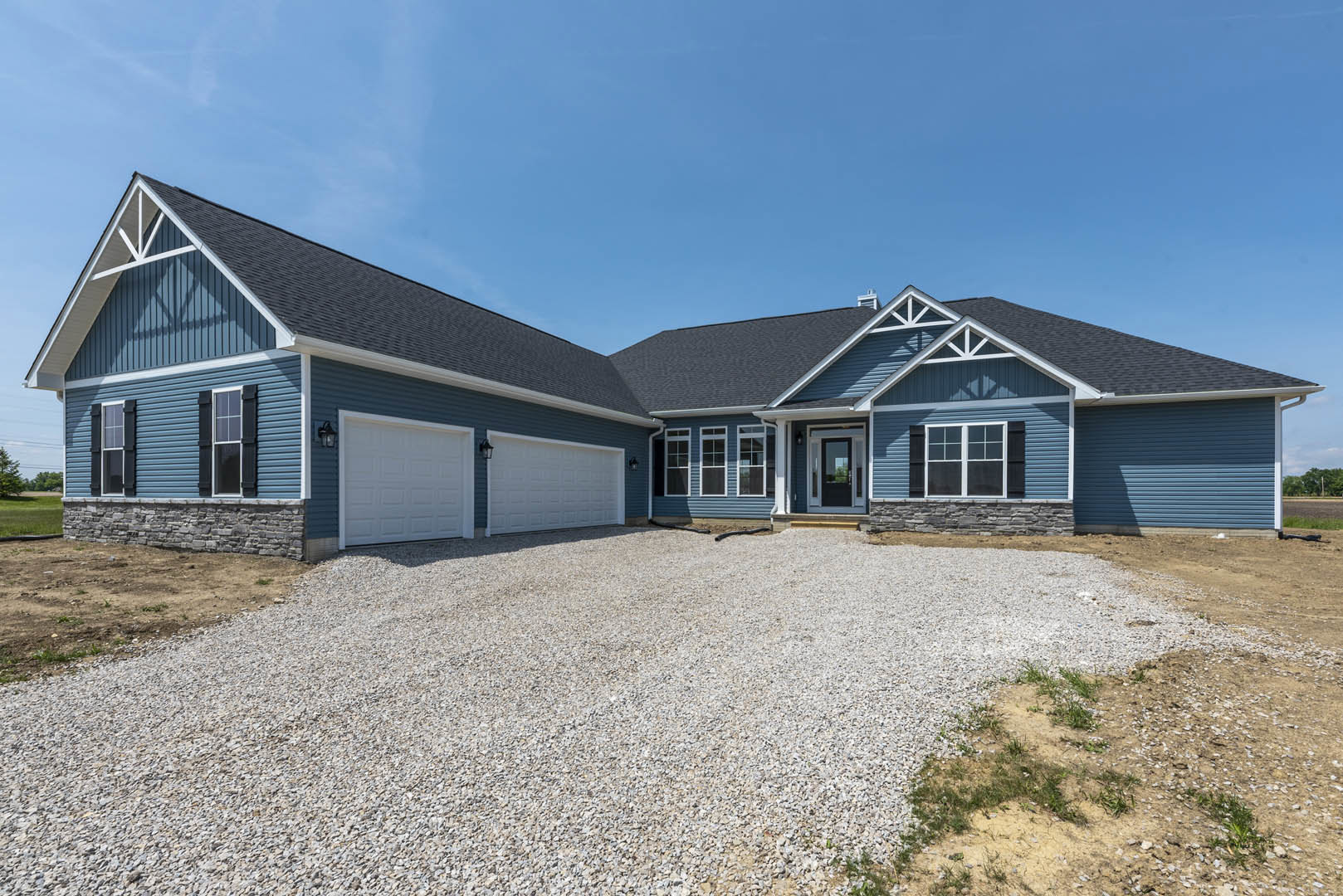 Two-story house with white siding, gravel driveway leading to a white garage door, exterior light fixture beside the garage, front window under a gabled roof, cloudy sky overhead