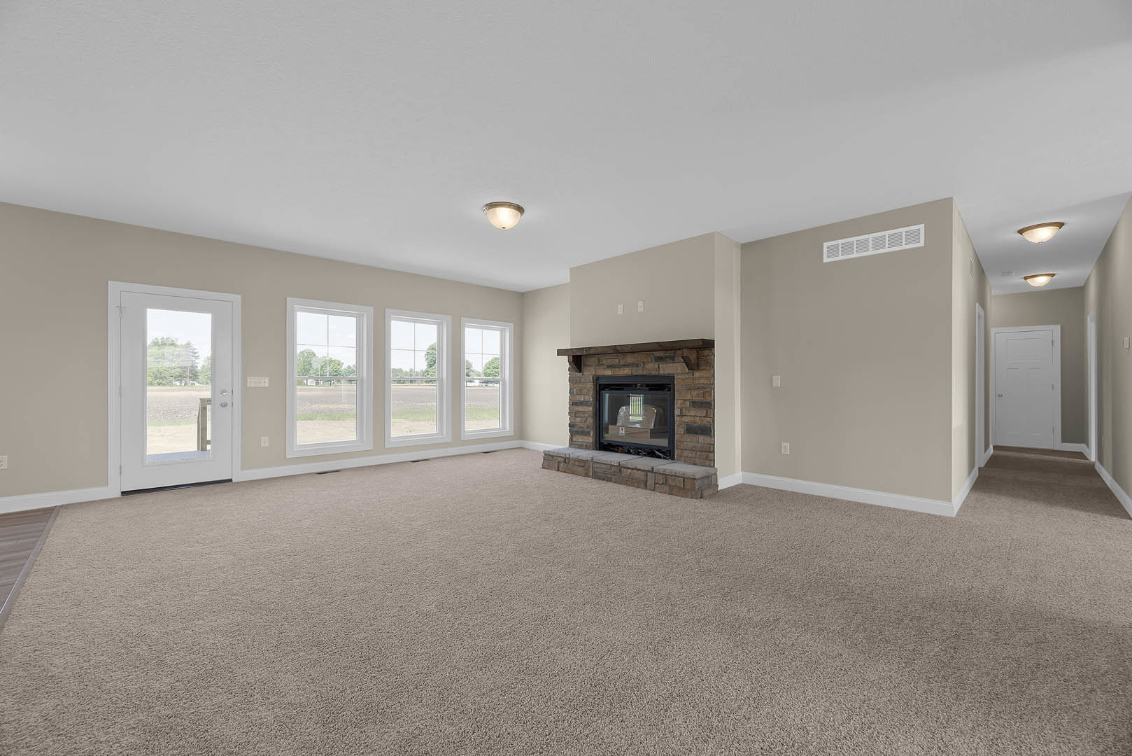 Living room with plush carpet, stone fireplace with glass doors, large window reflecting a chair, white door with glass panels, view of trees through window