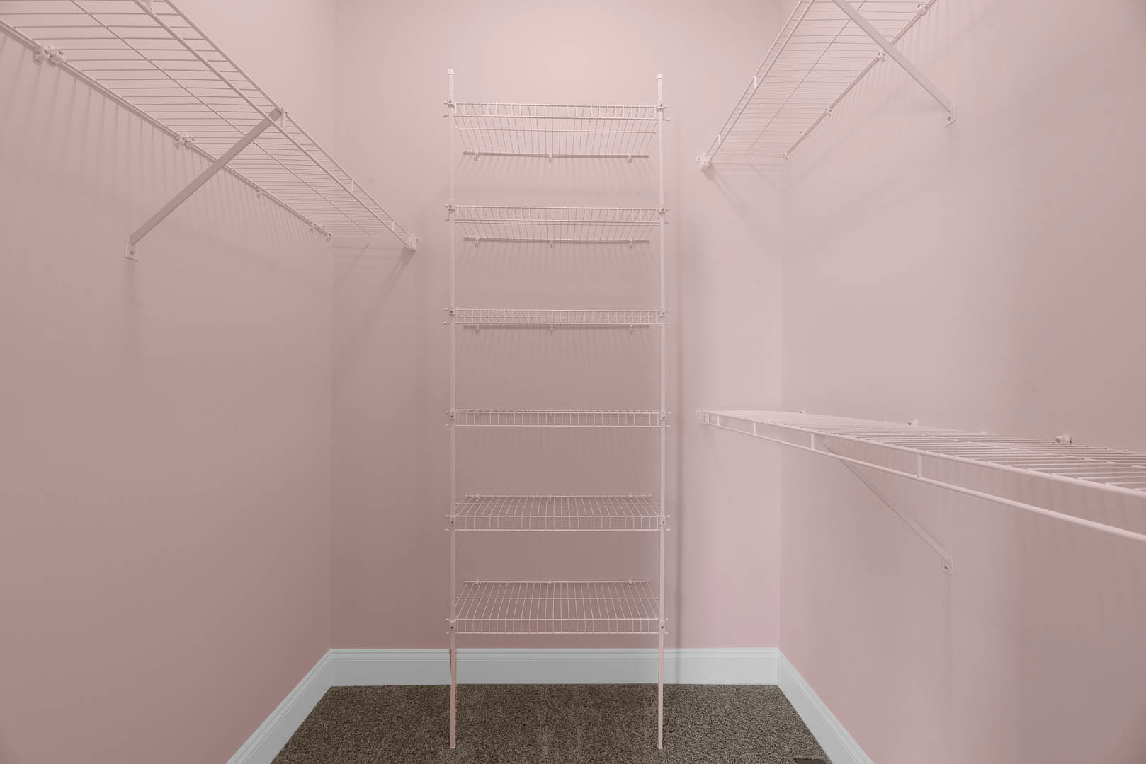 White wire shelves mounted on a pink plaster wall in a bathroom, with a close-up of a brown countertop surface.