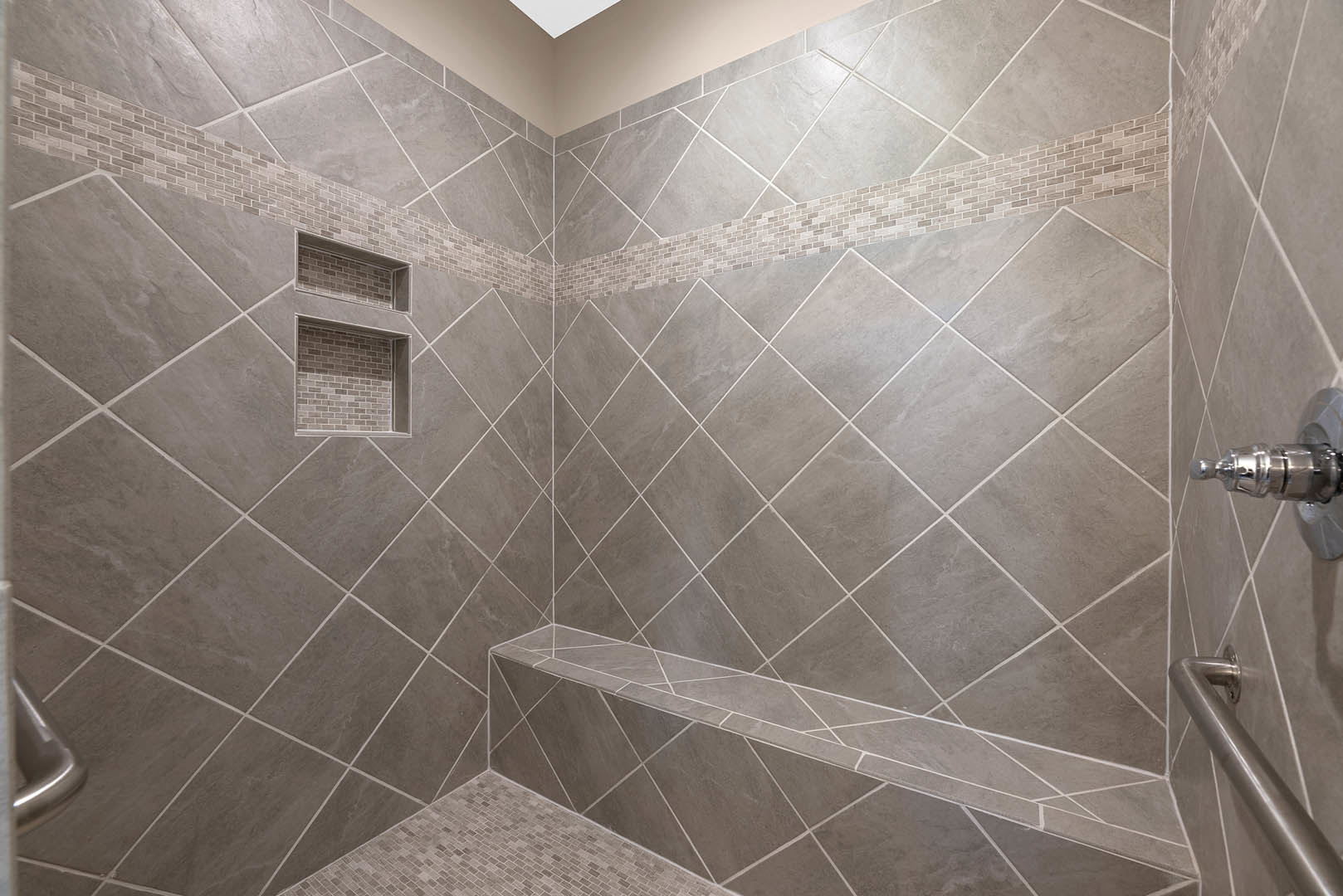 Tile shower with built-in bench, marble tile walls, metal faucet, and glass enclosure