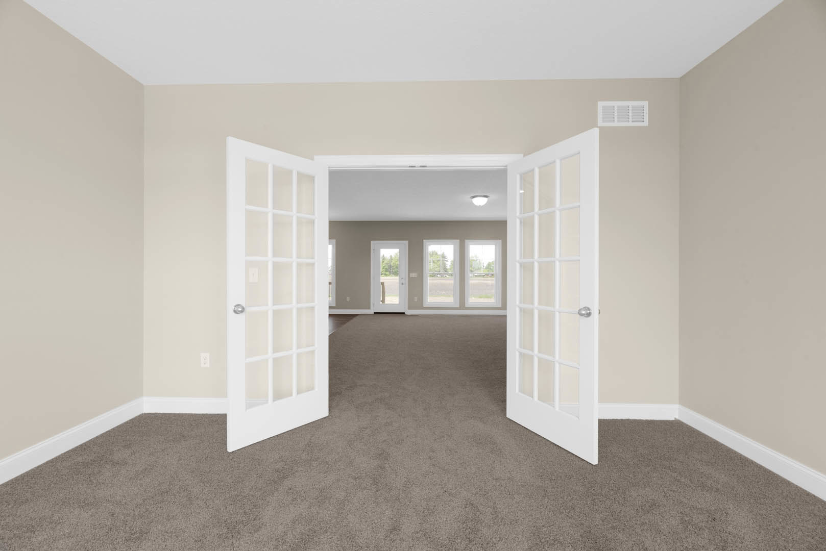 Laminate flooring and white plaster walls in a room with white paneled doors, one open to reveal glass panes and a view of green trees, white molding and a vent visible.