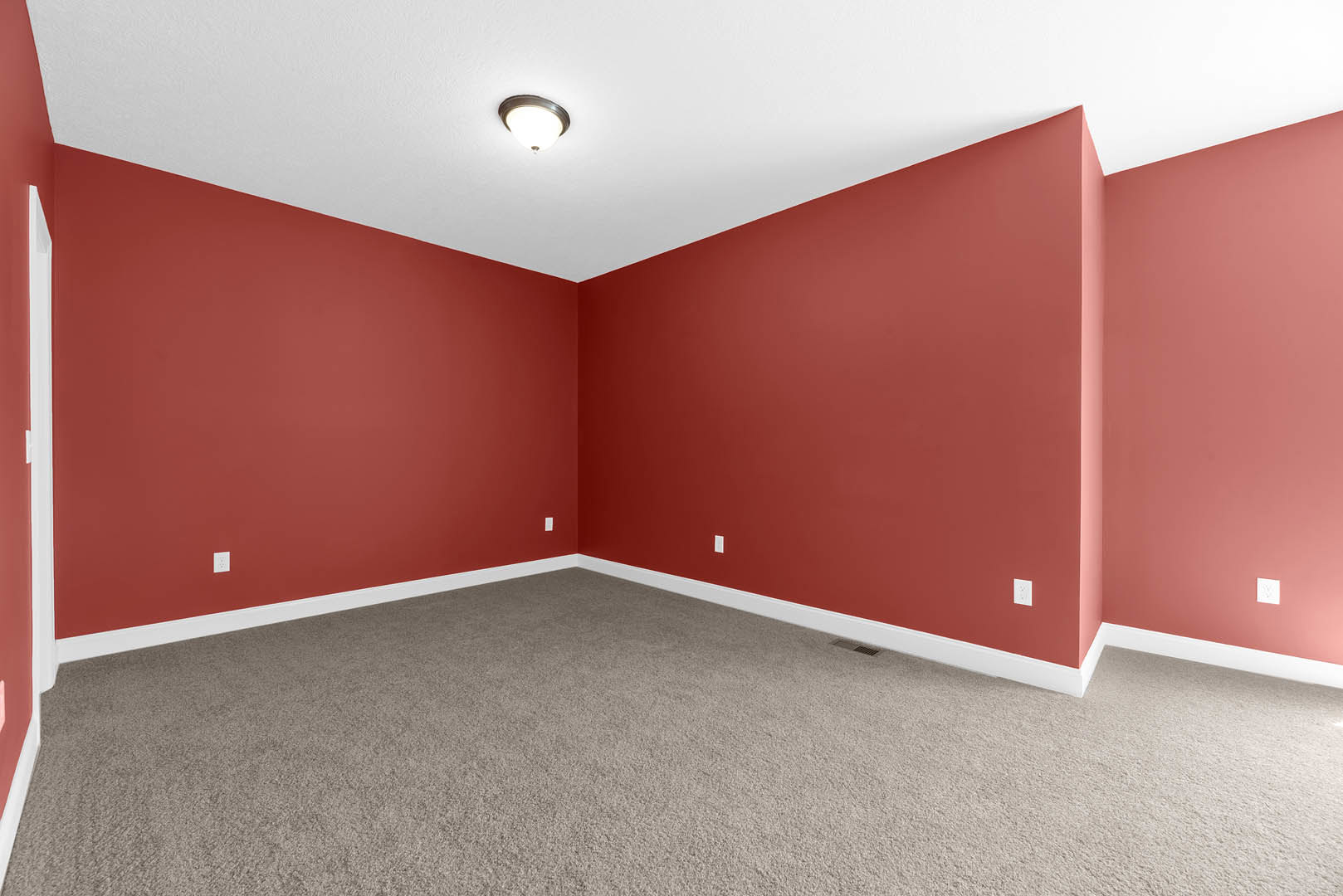 Red walls and red carpet in a residential room with a ceiling light fixture, plaster ceiling, and laminate flooring visible.
