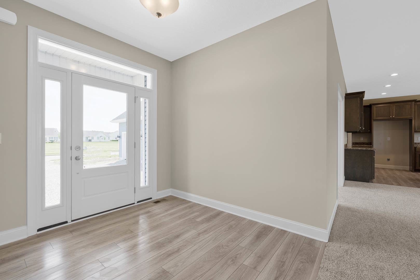 Hallway with wood flooring and white trim, white door with glass panes, glass door leading to adjacent room, close-up of modern light fixture, black rectangular object with white