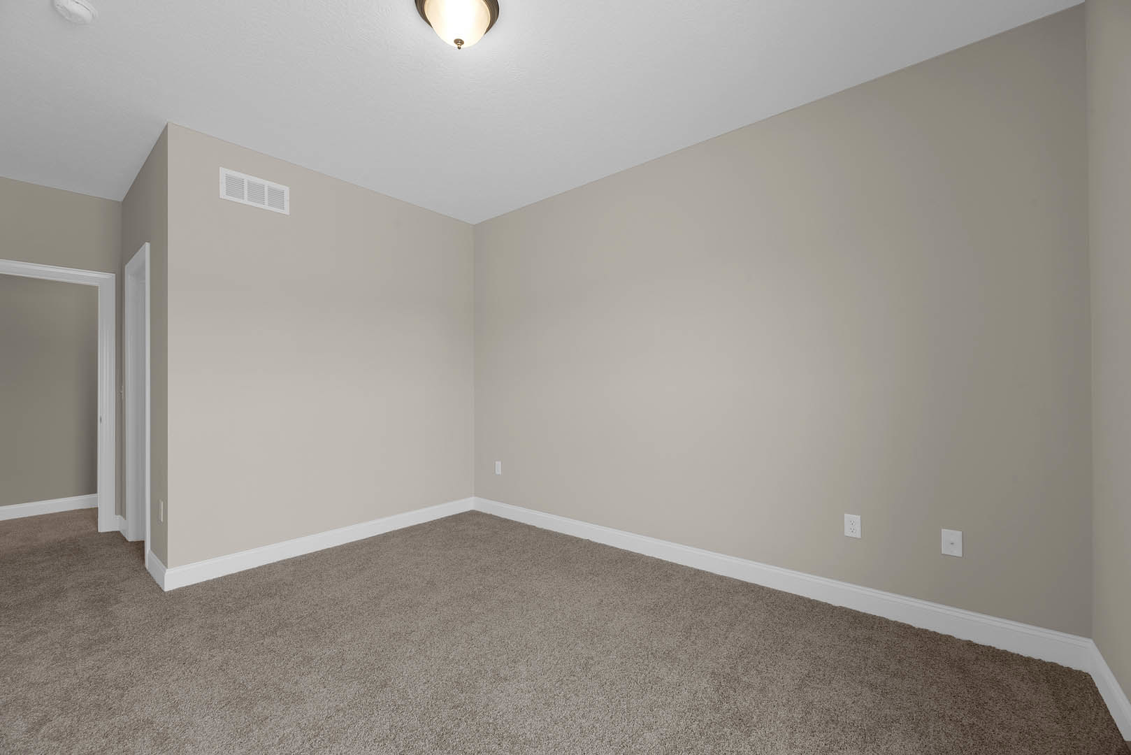 Neutral-toned room with white walls, ceiling-mounted light fixture, laminate flooring, white door frame, and wall vent