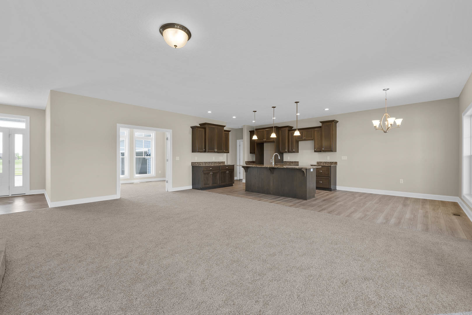 Spacious open-concept living area featuring a central kitchen island with laminate countertop, carpeted flooring throughout, white plaster walls, ceiling molding, and modern