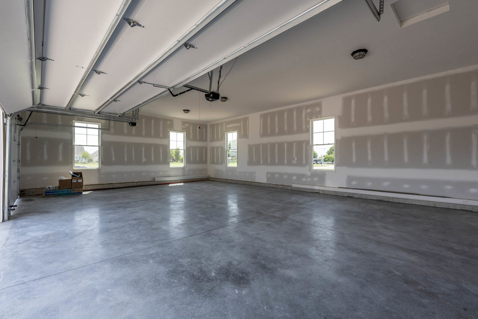 White plaster walls, polished concrete floor, ceiling light fixture, large window framing leafy trees and neighboring house