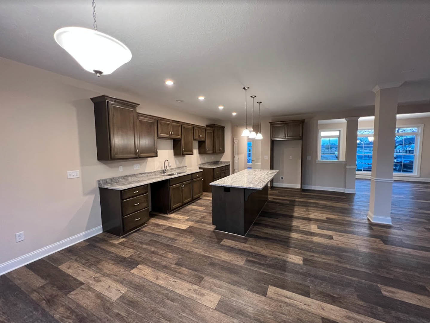 Kitchen with wide-plank wood flooring, large marble-topped island, white cabinetry, stainless steel sink, and pendant light fixture above island