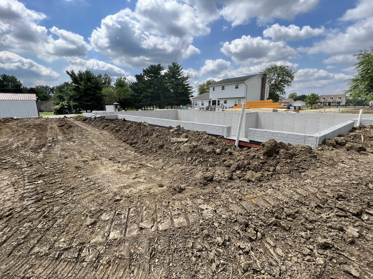 White brick house under construction with dirt piles in foreground, few windows, trees and clouds in background