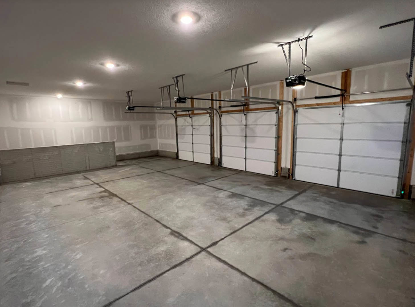 Spacious room with smooth white plaster walls, concrete grid-patterned floor, white garage door framed in metal, exposed ceiling pipes, and a person standing near the entrance