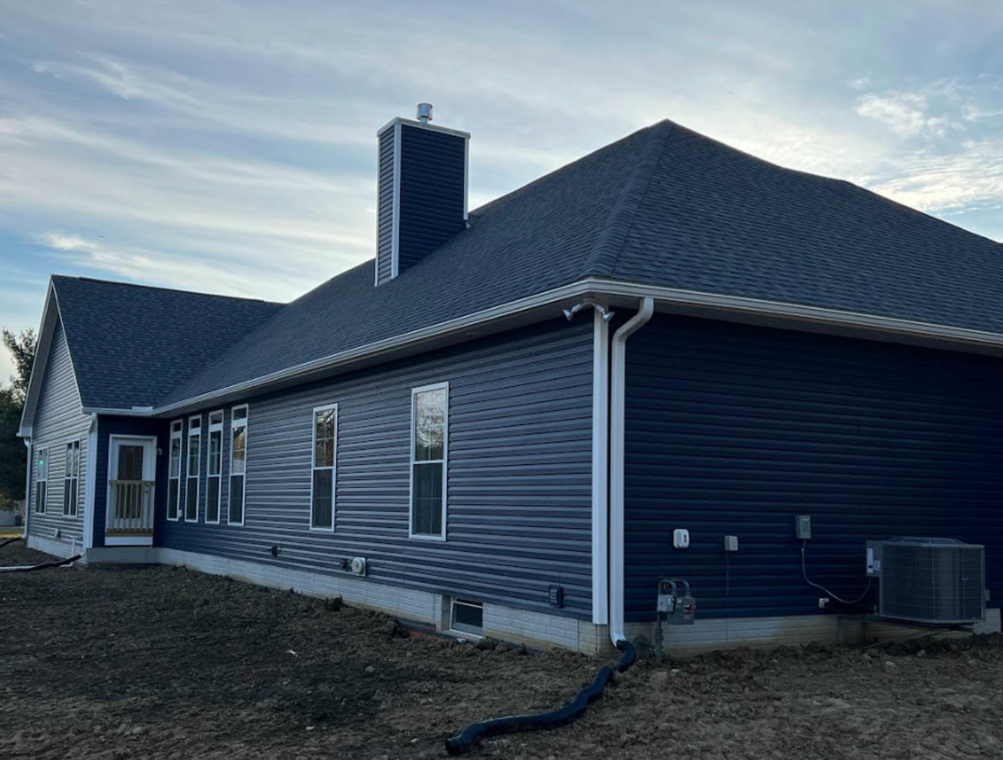 Blue horizontal siding exterior with white-framed windows, brick chimney, metal window railing, and black snake on the ground in front of the house